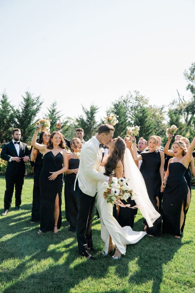 Bride and groom kissing surrounded by wedding party during outdoor summer wedding at Renault Winery in New Jersey